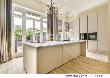 A sleek modern kitchen featuring contemporary cabinetry, elegant lighting, and large windows bringing natural light into the space. A sleek modern kitchen featuring contemporary cabinetry, elegant lighting, and large windows bringing natural light into the space. 123339302