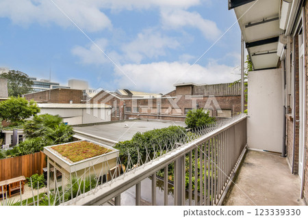 A scenic view from an urban balcony showcasing lush greenery, modern buildings, and a blue sky. The image captures the serene contrast of nature within a city backdrop. 123339330