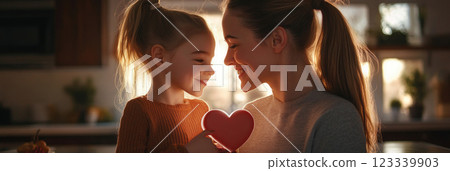 A joyful moment between a mother and daughter in a cozy kitchen, sharing a heart drawing, with natural decor creating a warm, loving atmosphere, banner 123339903