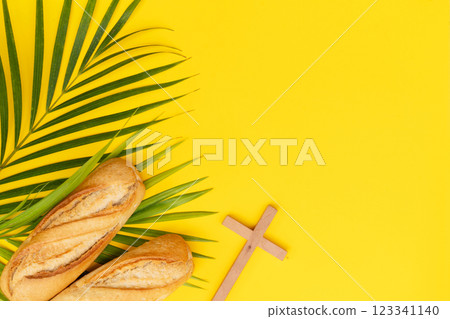 A wooden cross with a Bible and bread on a palm leaves pattern, a Palm Sunday theme A wooden cross with a Bible and bread on a palm leaves pattern, a Palm Sunday theme 123341140