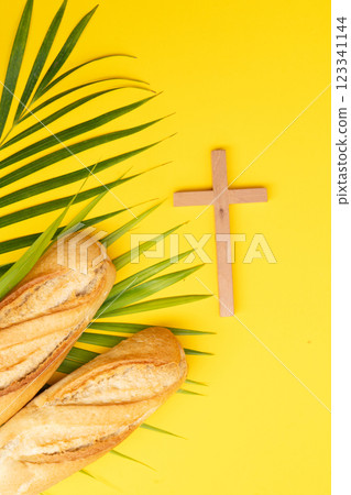 A wooden cross with a Bible and bread on a palm leaves pattern, a Palm Sunday theme 123341144