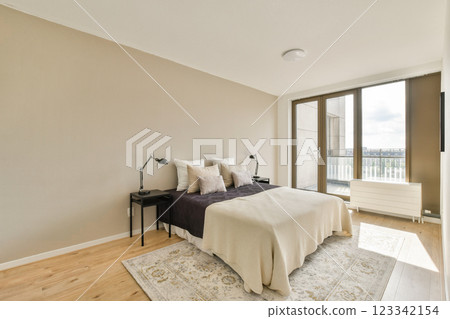 A stylish modern bedroom featuring a neutral color palette, cozy bedding, and large windows that provide natural light, creating a serene atmosphere. 123342154