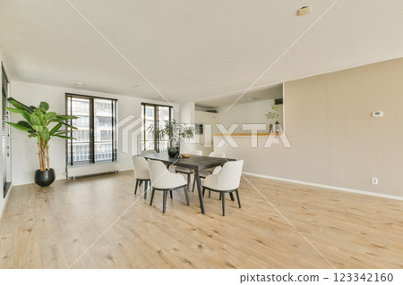 A stylish, modern dining area featuring a wooden table, elegant chairs, and a large potted plant, illuminated by natural light streaming through windows. A stylish, modern dining area featuring a wooden table, elegant chairs, and a large potted plant, illuminated by natural light streaming through windows. 123342160