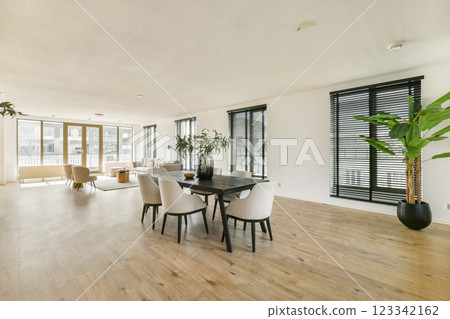 A spacious modern dining and living area with natural light, featuring elegant furniture and indoor plants that enhance the ambiance. 123342162