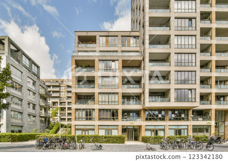 A contemporary residential building featuring a minimalist design and ample balconies, surrounded by greenery and a paved pathway. A contemporary residential building featuring a minimalist design and ample balconies, surrounded by greenery and a paved pathway. 123342180