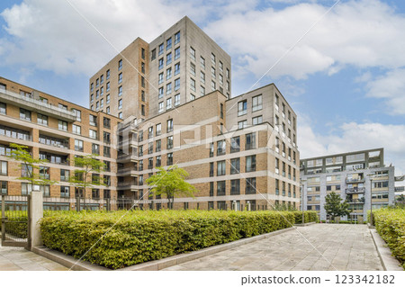A contemporary residential building complex showcasing sleek architecture and greenery, complemented by a blue sky dotted with clouds. A contemporary residential building complex showcasing sleek architecture and greenery, complemented by a blue sky dotted with clouds. 123342182