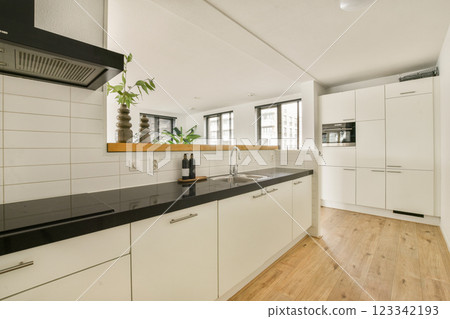 A contemporary kitchen featuring minimalist cabinetry, a black countertop, and ample light from large windows. The clean lines create a spacious, inviting atmosphere. 123342193