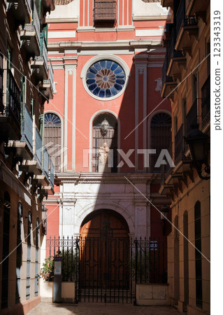 The image shows a view of a narrow alley leading to a brightly colored building, which appears to be a church or religious structure given the presence of a cross at the top and the architectural 123343319