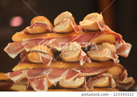 This image shows a stack of sandwiches. Each sandwich looks to be made with a small baguette or a similar type of bread, cut in half, and filled with slices of ham. The arrangement of sandwiches is 123343322