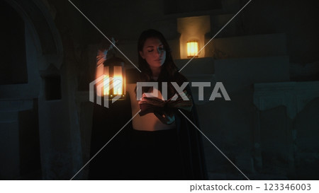 Woman Reads Mysteries On Magic Book In Ancient Cave At Night With Lantern Woman Reads Mysteries On Magic Book In Ancient Cave At Night With Lantern 123346003