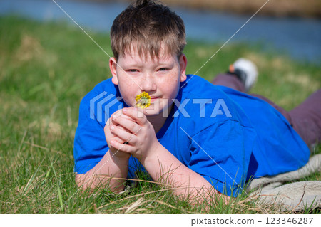 A teenage boy lies in a meadow and holds a dandelion in his hands. A teenage boy lies in a meadow and holds a dandelion in his hands. 123346287