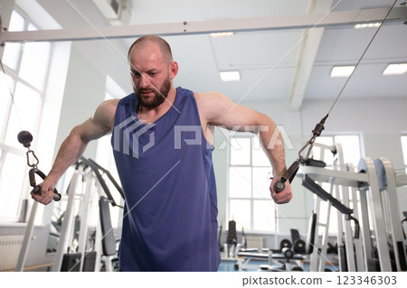 Male athlete bodybuilder exercising in the gym. Strength training on a cable machine. 123346303