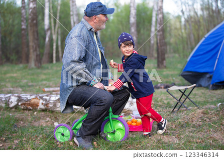 Grandfather and grandson are having fun playing with a bicycle in nature. 123346314