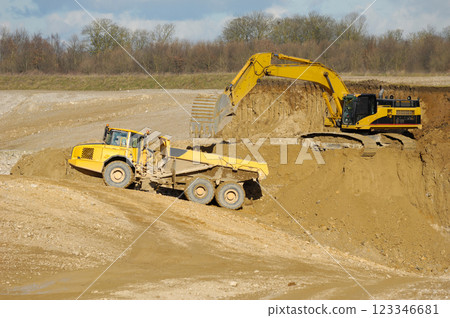 Yellow dump trucks and excavator are working in gravel pit 123346681