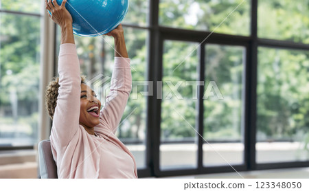 Happy older person raised a blue fitness ball, a person exercising in a comfortable environment, fitness-oriented therapy promoting active aging and health in older adults 123348050