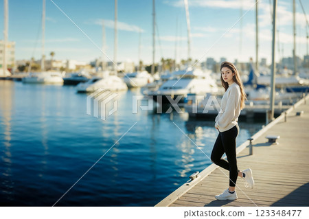 Young woman standing on pier in marina on the background of magnificent yachts, active seaside vacation and yacht trip, summer regatta in Mediterranean Sea 123348477