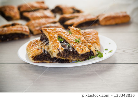 Golden puff pastries with mushroom filling and sesame seeds, on a light wooden table Golden puff pastries with mushroom filling and sesame seeds, on a light wooden table 123348836