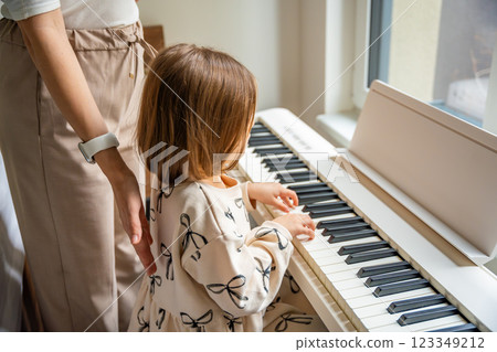 Home lesson with teacher on music for girl on white piano synthesizer. Concept of early development: learning music enhances motor skills, hearing, intelligence, fostering creativity from childhood Home lesson with teacher on music for girl on white piano synthesizer. Concept of early development: learning music enhances motor skills, hearing, intelligence, fostering creativity from childhood 123349212