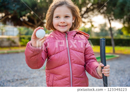 Portrait of Little girl Holding in hand Mini-Golf Ball. Little girl playing mini golf outdoor. Family vacations or resort. 123349223