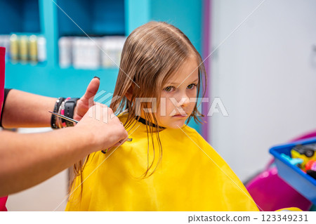 Hairdresser making a hair style to cute little girl in real child salon with colorful interior and toys 123349231