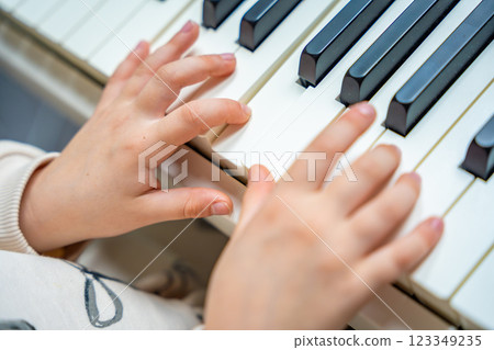 Close up view of small hands of girl on white piano synthesizer. Concept of early development: learning music enhances motor skills, hearing, and intelligence, fostering creativity from childhood 123349235