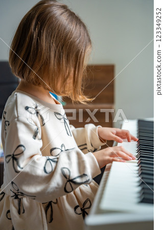 Home lesson on music for the girl on white piano synthesizer. Concept of early development: learning music enhances motor skills, hearing, and intelligence, fostering creativity from childhood Home lesson on music for the girl on white piano synthesizer. Concept of early development: learning music enhances motor skills, hearing, and intelligence, fostering creativity from childhood 123349252