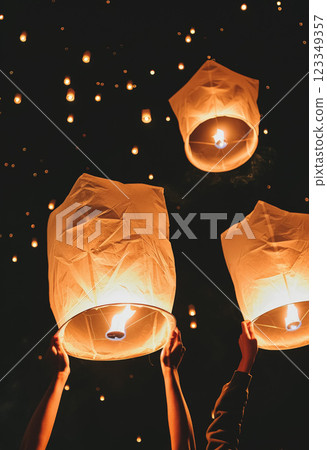 Glowing paper lanterns float into night sky during festive gathering, symbolizing hope and unity, as people release them in warm, communal celebration 123349357