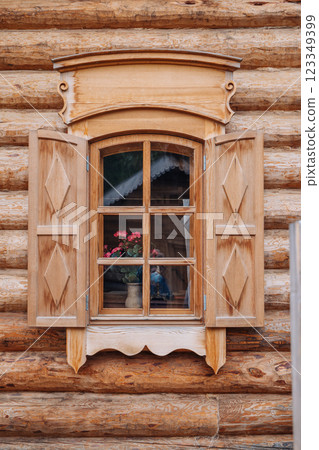 Open wooden shutters framing a window with pink geraniums in a traditional russian log house, showcasing architectural heritage 123349399