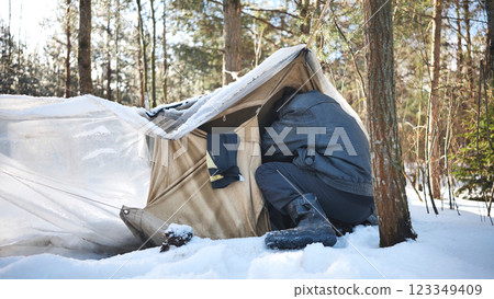 Homeless man seeking refuge from cold entering makeshift tent in snowy forest, depicting poverty and social issues 123349409