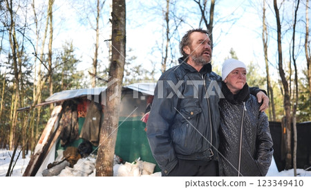 Alcohol addicted homeless couple standing near their makeshift shelter in a snowy forest, facing an uncertain future 123349410