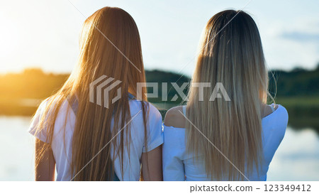 Two school girlfriends with long hair enjoying a stunning sunset while taking in the tranquil beauty of a lake and surrounding landscape Two school girlfriends with long hair enjoying a stunning sunset while taking in the tranquil beauty of a lake and surrounding landscape 123349412