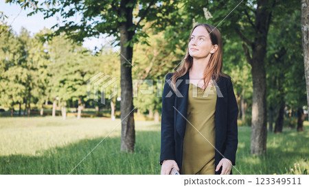 Young businesswoman walking in a green park during her break, enjoying the fresh air and looking up at the trees Young businesswoman walking in a green park during her break, enjoying the fresh air and looking up at the trees 123349511