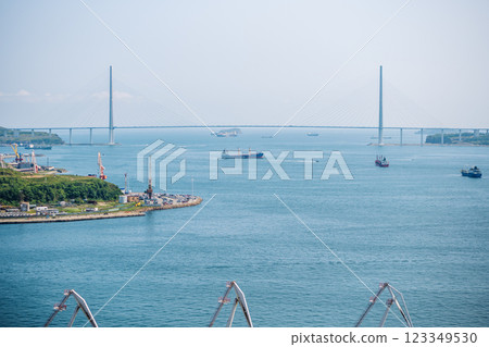 Cargo ships sailing gracefully beneath the russian bridge on a bright, sunny day, creating a vital connection between two islands Cargo ships sailing gracefully beneath the russian bridge on a bright, sunny day, creating a vital connection between two islands 123349530