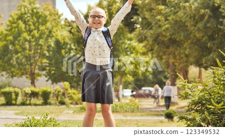 Excited schoolgirl jumping with arms raised in celebration after school, enjoying freedom and happiness in a park 123349532