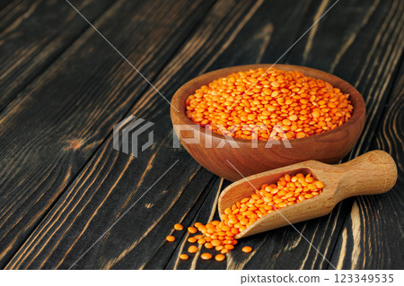 Red lentils are spilling from wooden scoop next to bowl full seeds, creating a rustic and healthy food scene 123349535