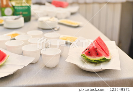 There are pieces of watermelon and clean white cups on the table. 123349571