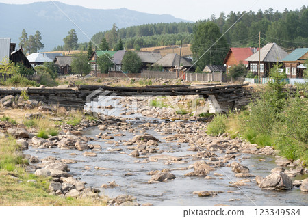 Weathered wooden bridge spanning rocky river between mountain slopes, connecting secluded village nestled amid verdant landscape Weathered wooden bridge spanning rocky river between mountain slopes, connecting secluded village nestled amid verdant landscape 123349584