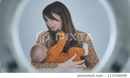 Mother cradling infant daughter, backlit by ring light, creating soft bokeh and warm family moment 123349696