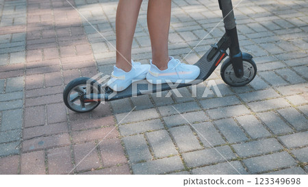 Teen girl riding electric scooter, legs in view, enjoying sunlit park path with eco friendly urban mobility 123349698