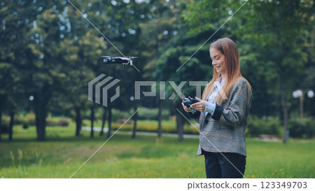 Female entrepreneur piloting drone, operating remote control in verdant park setting Female entrepreneur piloting drone, operating remote control in verdant park setting 123349703