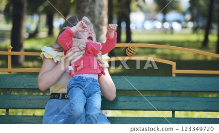 Caring mother comforting weeping child on park bench during bright summer afternoon Caring mother comforting weeping child on park bench during bright summer afternoon 123349720