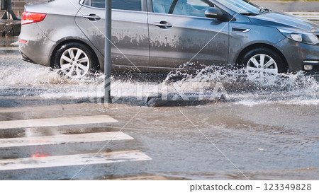 Gray car splashing through flooded street after heavy rain, creating large spray of water 123349828