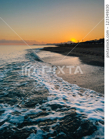 Gentle ocean waves washing over rocky shoreline, vibrant orange sunrise illuminating distant mountainous landscape with serene coastal scenery Gentle ocean waves washing over rocky shoreline, vibrant orange sunrise illuminating distant mountainous landscape with serene coastal scenery 123349830