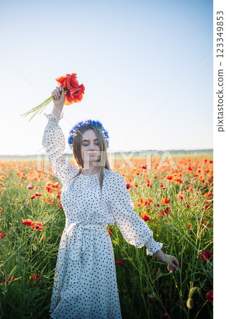 Woman in white dress, floral crown, standing amid blooming poppy field, basking in golden summer sunlight Woman in white dress, floral crown, standing amid blooming poppy field, basking in golden summer sunlight 123349853
