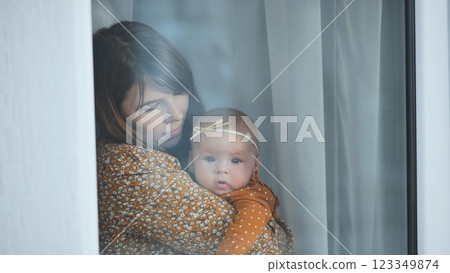 Mother holding her newborn baby girl, standing by the window, enjoying a quiet moment of connection and love 123349874