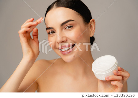 Smiling Woman Applying Face Cream Skincare With a Cream Container 123350156