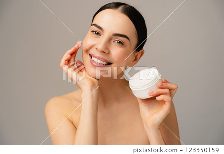 Woman Smiling While Holding Skincare Cream in Minimalist Studio Lighting 123350159