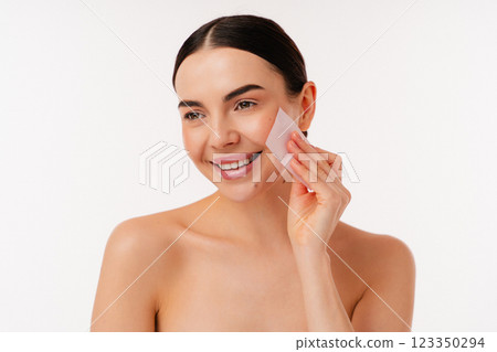 Smiling Woman Cleansing Skin with Blotting Paper on Light Background Smiling Woman Cleansing Skin with Blotting Paper on Light Background 123350294