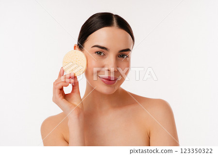 Young Woman Demonstrating Facial Skincare with Exfoliating Sponge on White Background Young Woman Demonstrating Facial Skincare with Exfoliating Sponge on White Background 123350322