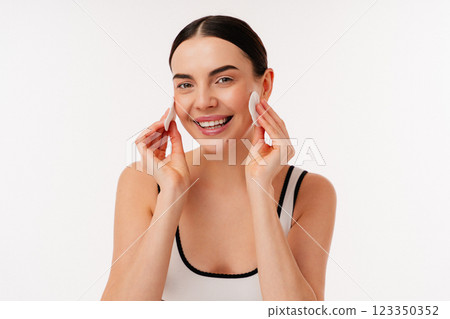 Smiling Woman Cleansing Skin With Cotton Pads in White Studio Background 123350352